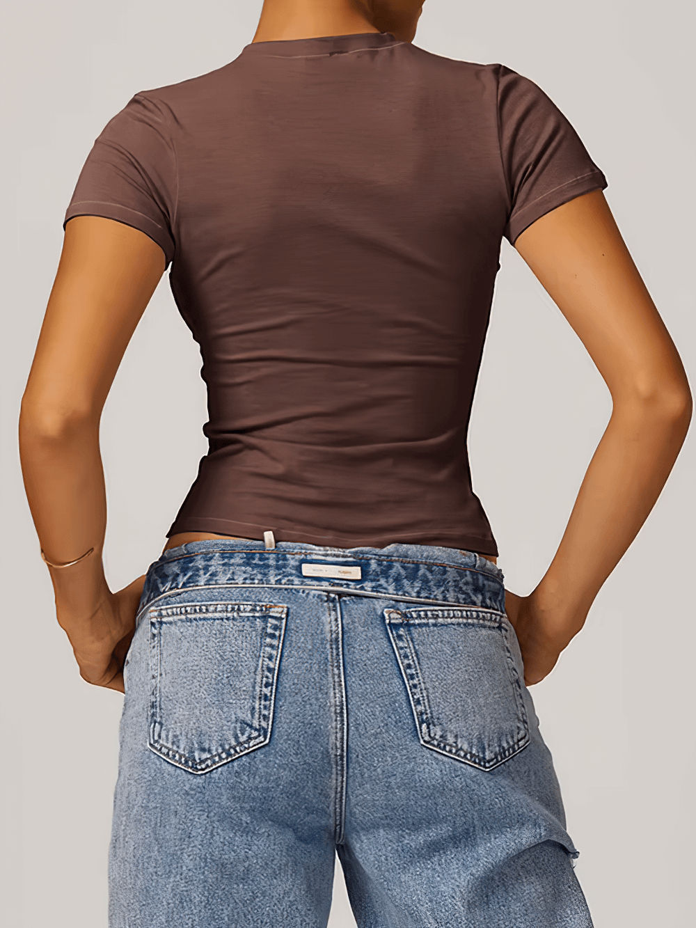 Back view of a woman wearing a brown stylish short-sleeve yoga t-shirt and blue jeans, showcasing a trendy and flexible fit for sports.