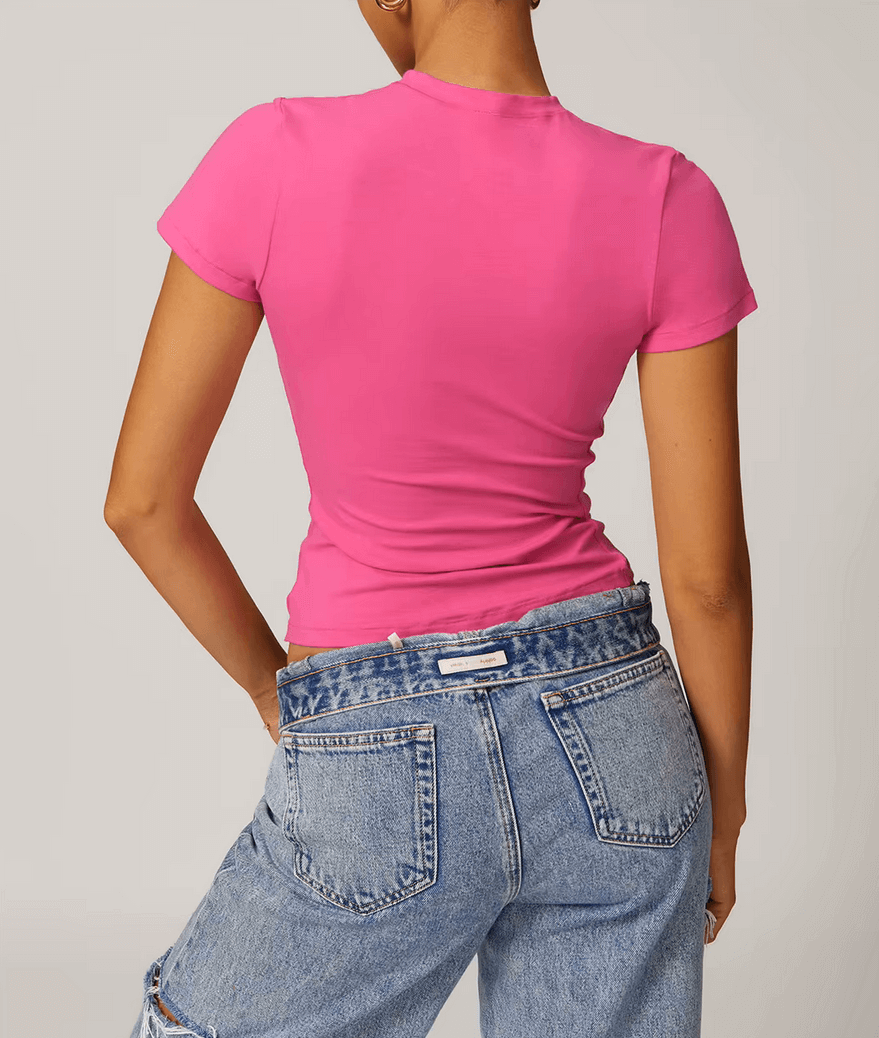 Back view of woman wearing stylish pink short-sleeve yoga t-shirt with blue jeans, highlighting trendy and comfortable fit for active wear.