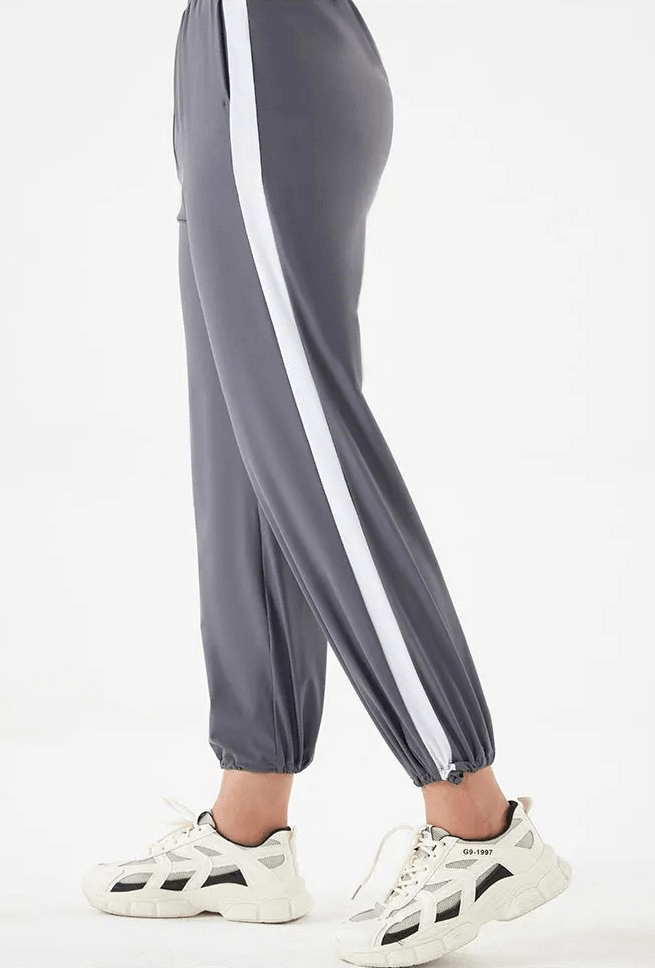Gray women's track pants with white stripes, perfect for yoga and workouts, paired with stylish white sneakers on a white background.