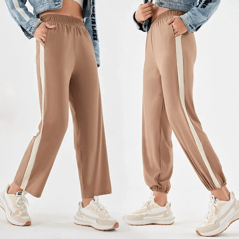 Chic women's track pants with white stripes, perfect for yoga and active wear; full-length, camel color, paired with casual sneakers.