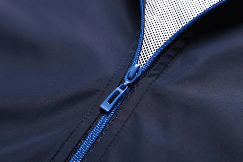 Close-up of a blue zipper on a stylish men's polyester tracksuit with a mandarin collar and sleek patchwork design.