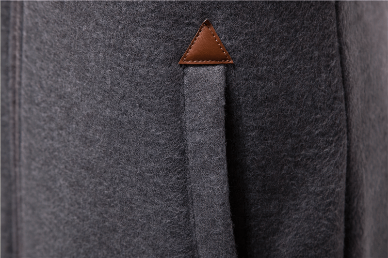 Close-up of dark grey fabric with a small brown leather triangle detail, showcasing texture and stylish design.