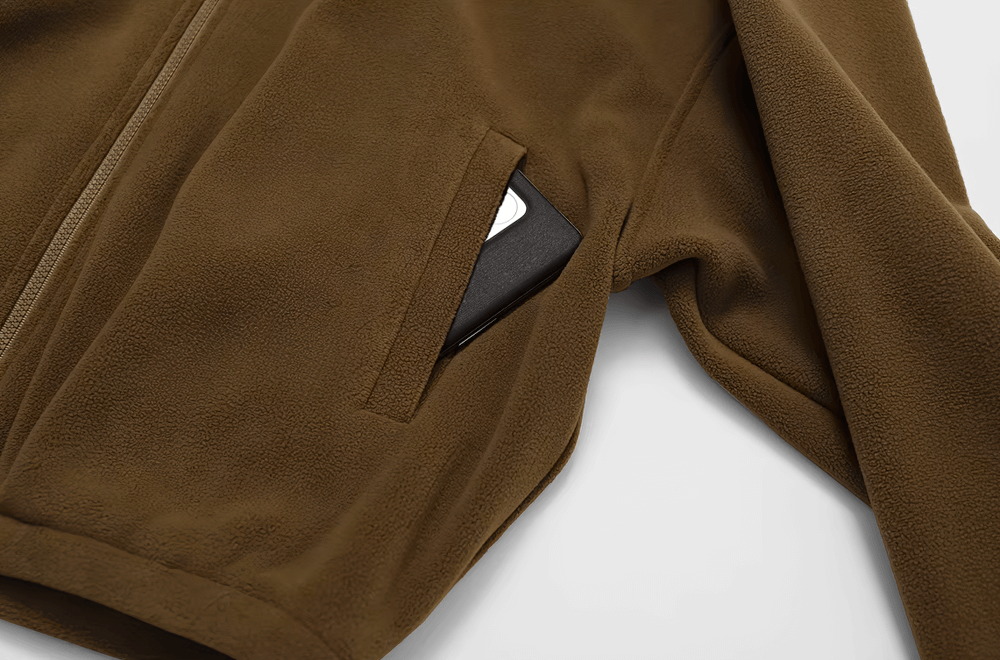 Close-up of stylish anti-pilling fleece jacket in brown with a slit pocket holding a smartphone, perfect for outdoor activities.