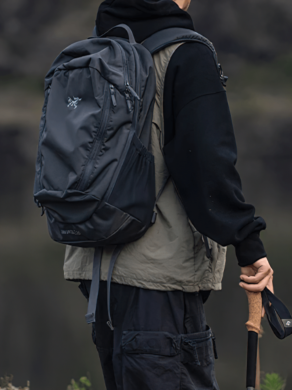 Man wearing gray tactical utility vest with multi-pocket design, carrying a backpack on an outdoor adventure.