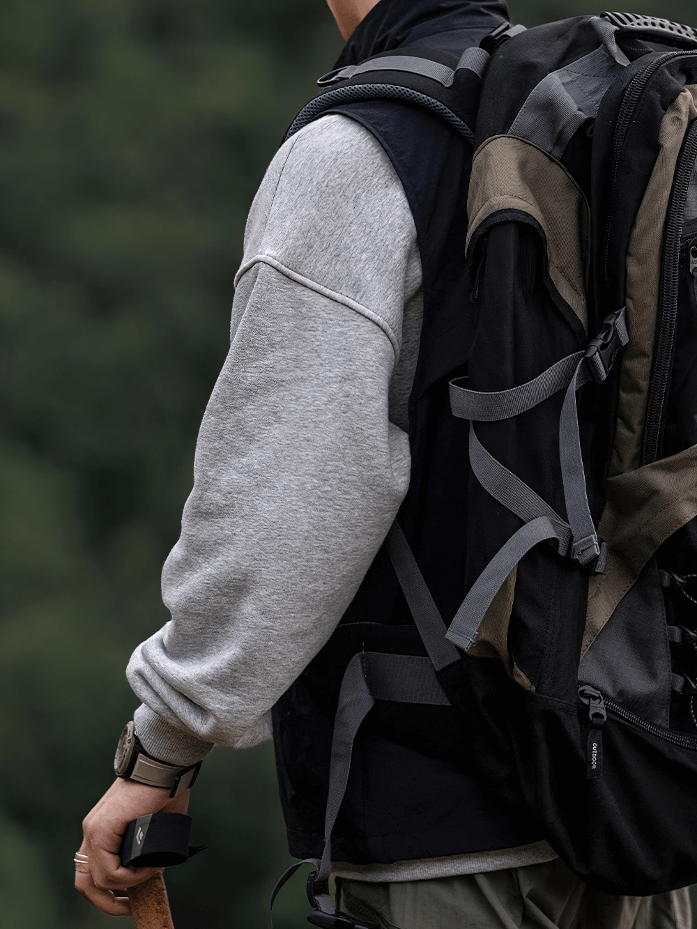 Man wearing tactical utility vest with multi-pocket design holding a hiking tool, perfect for outdoor adventures.