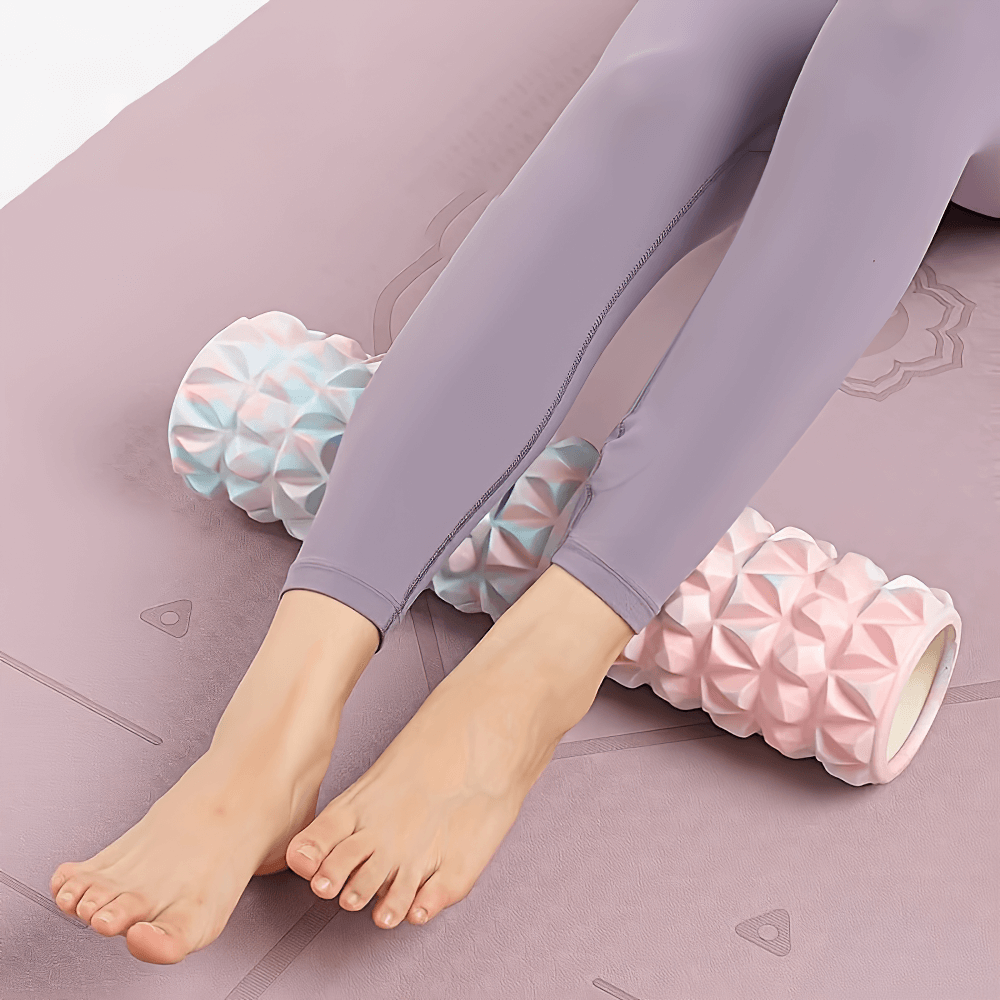 Person using a pink and blue textured foam roller for deep tissue massage on a yoga mat, ideal for fitness and muscle recovery.