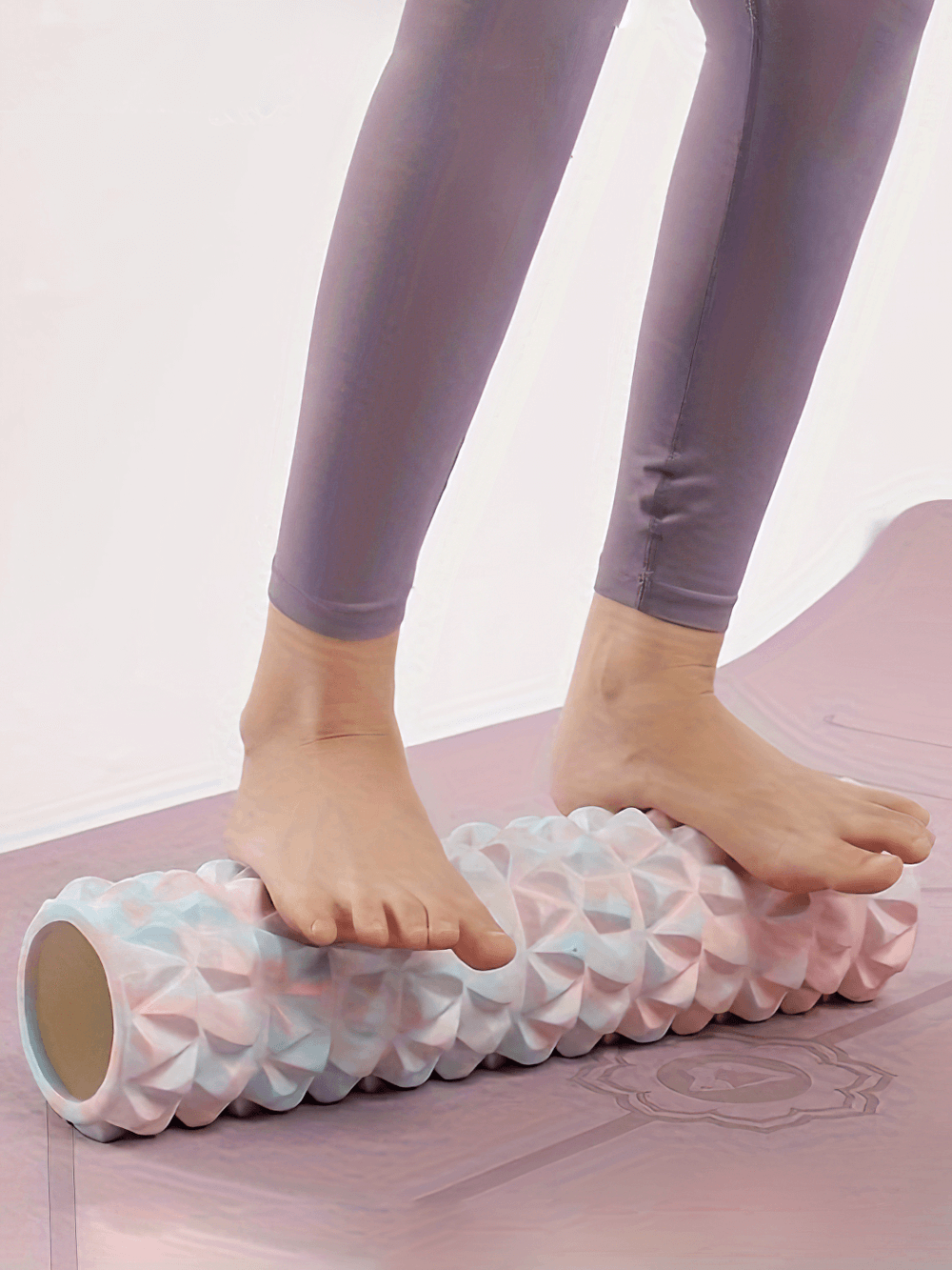 Person using textured foam roller on feet for deep tissue massage during yoga. Enhances flexibility and muscle recovery. SF2825 model in pink.