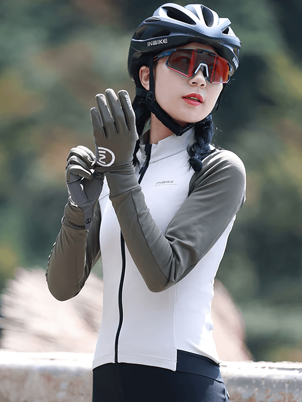 Woman wearing a thermal cycling jacket with full zipper and gloves, cycling outdoors, dressed for cool weather and safety with helmet.