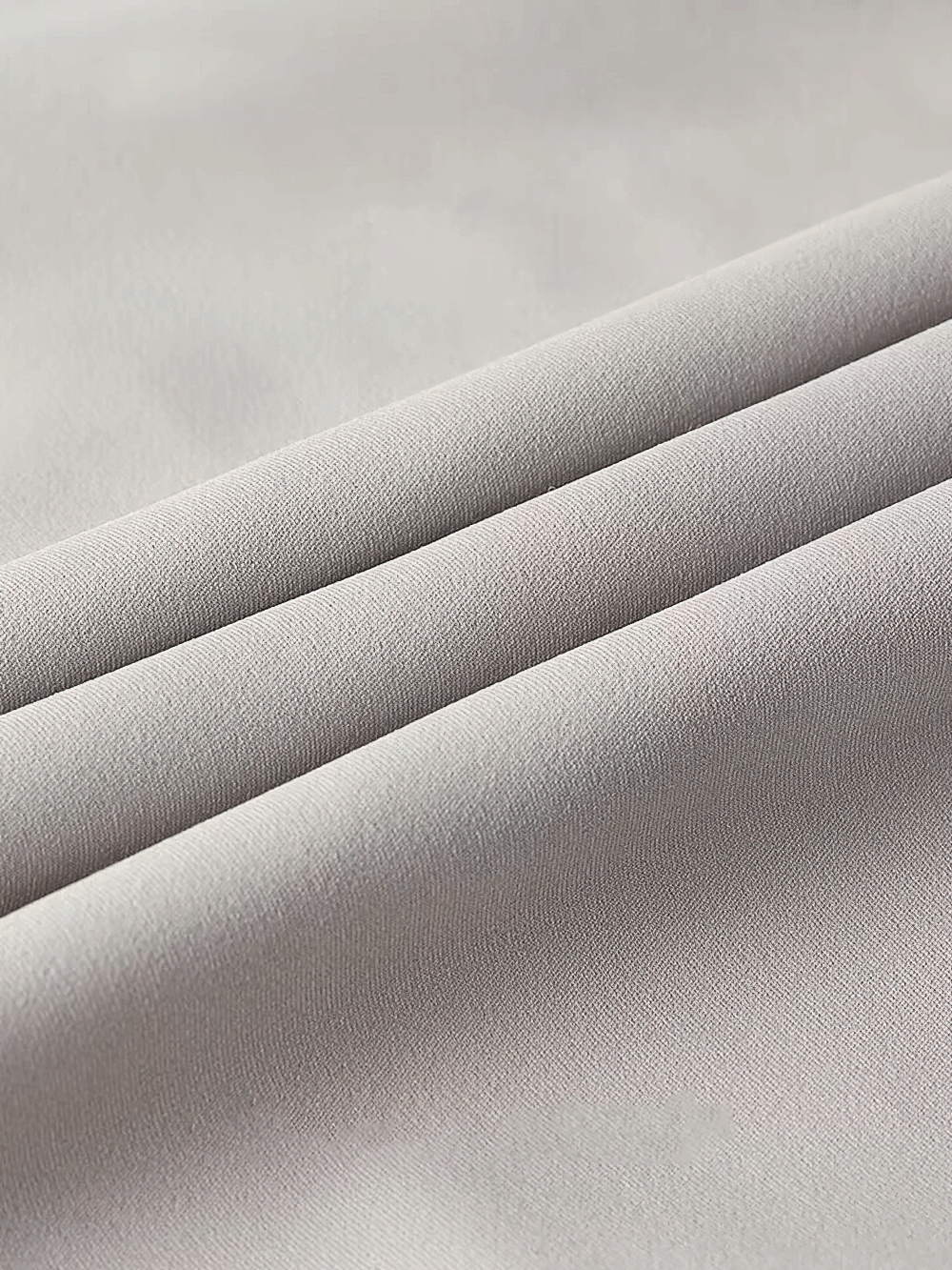 Close-up of light gray polyester fabric with a smooth and soft texture, ideal for making durable outdoor cycling jackets.