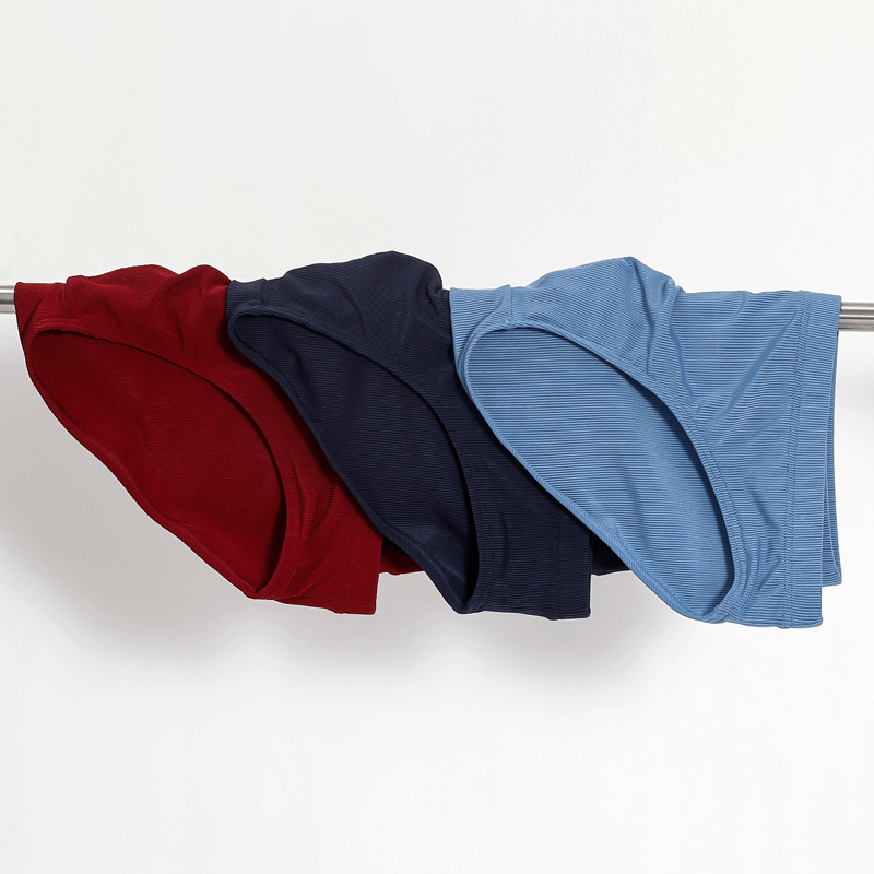 Thin breathable ribbed briefs for men in red, navy blue, and light blue, displayed on a rod, showcasing the stylish low-rise design.