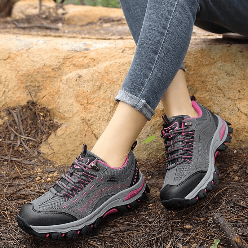 Women's trekking sneakers SF0232 with pink accents on a rocky trail, offering comfort, support, and grip for beginner hikers.