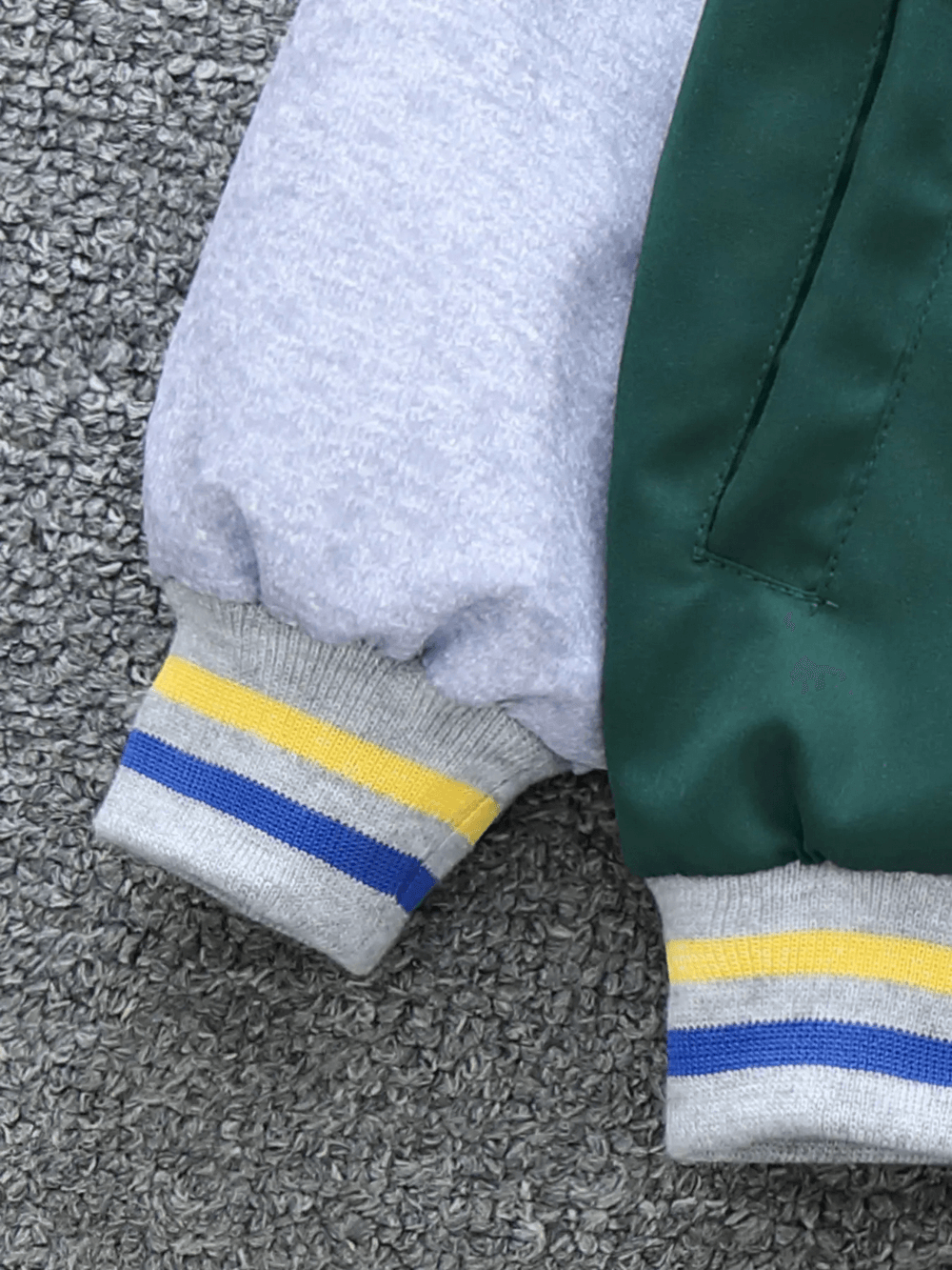 Close-up of a color-blocked baseball jacket sleeve with letter print detail, highlighting vibrant colors and sporty style for kids.