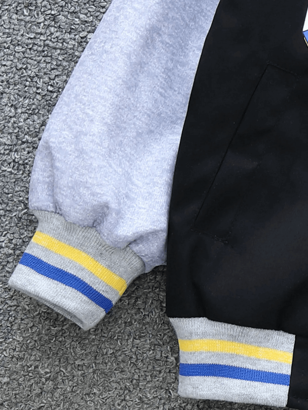 Close-up of trendy color-blocked baseball jacket sleeve with bold stripes, designed for stylish kids' casual wear.