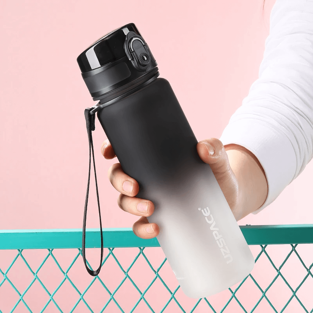 Hand holding black frosted Tritan sports water bottle with timeline, featuring bounce lid and leakproof design.