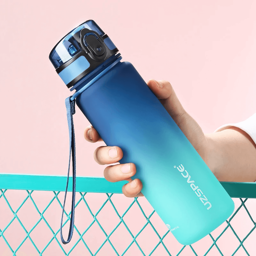 Blue Tritan sports water bottle with timeline, held over fence. Features bounce lid, leakproof design, and BPA-free materials for fitness.