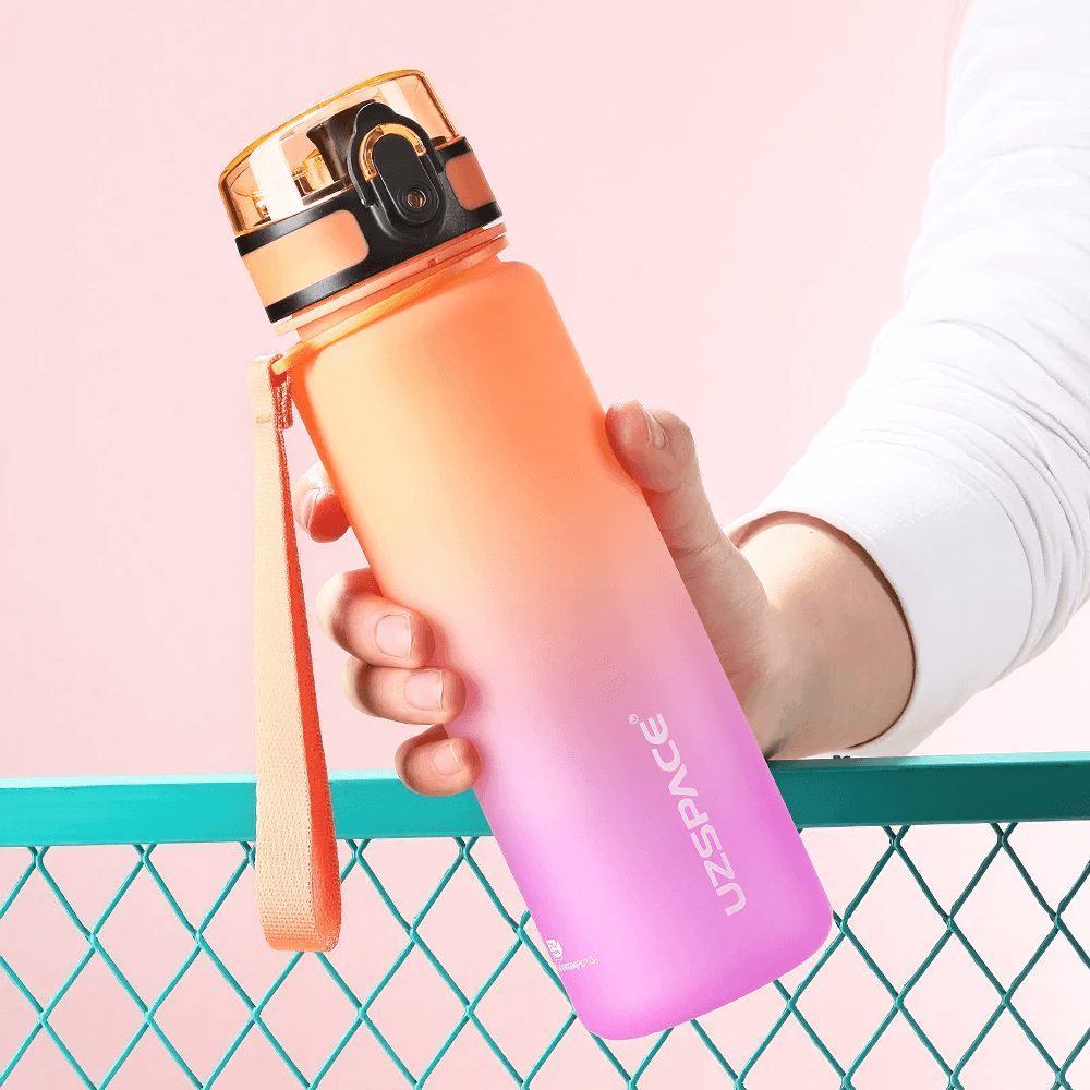 Person holding a pink and orange gradient Tritan sports water bottle with timeline and strap, perfect for fitness and outdoor activities.