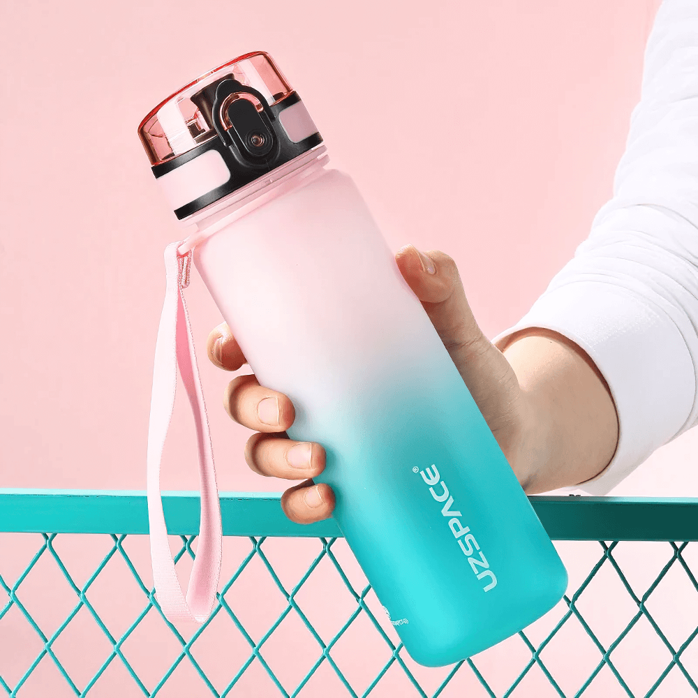 Trendy pink and teal Tritan sports water bottle with timeline reminder held against pastel background, perfect for outdoor fitness.