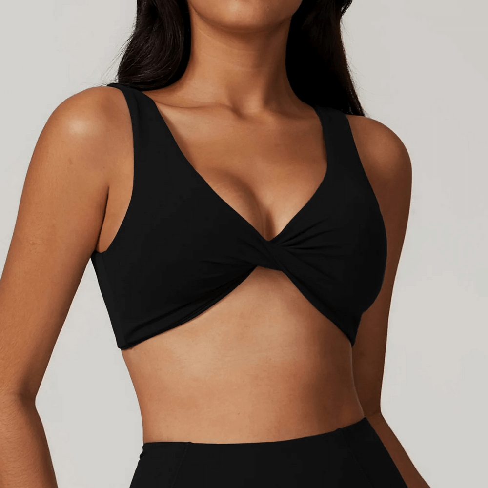 Woman wearing black twist front sports bra top for fitness with backless design, ideal for yoga and workouts. SF2450.