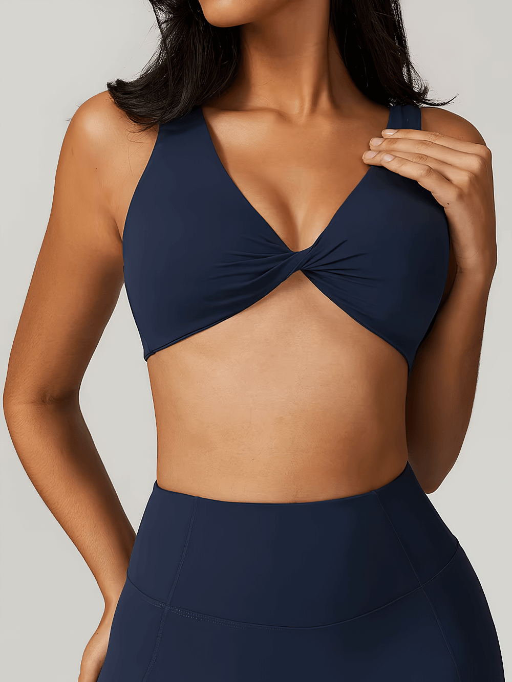 Woman wearing navy twist front sports bra top for fitness, yoga, and running. Stylish backless design with high support and quick-dry fabric.