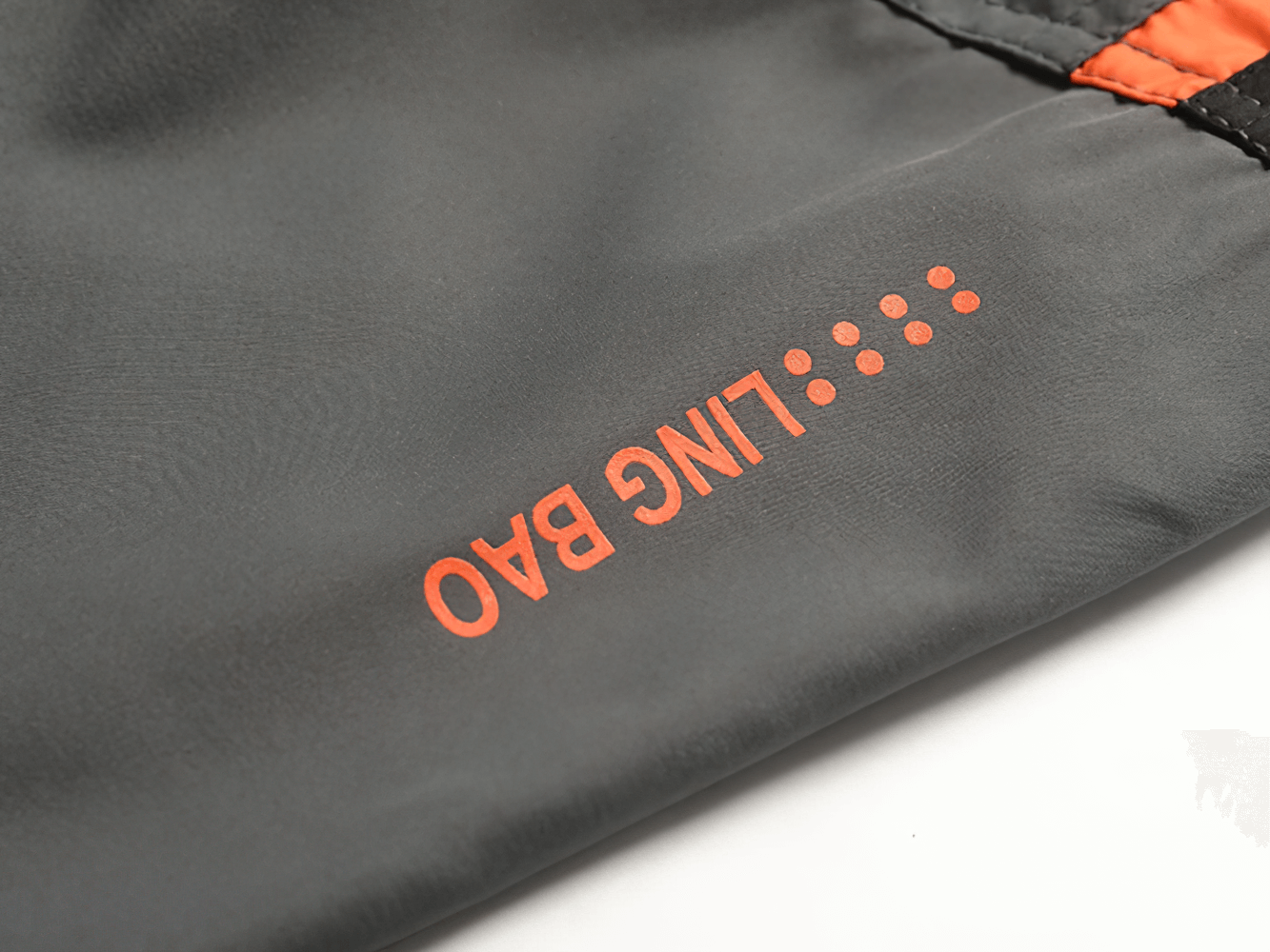 Close-up of a gray sports tracksuit with red accents featuring bold print in vibrant orange lettering on the fabric.