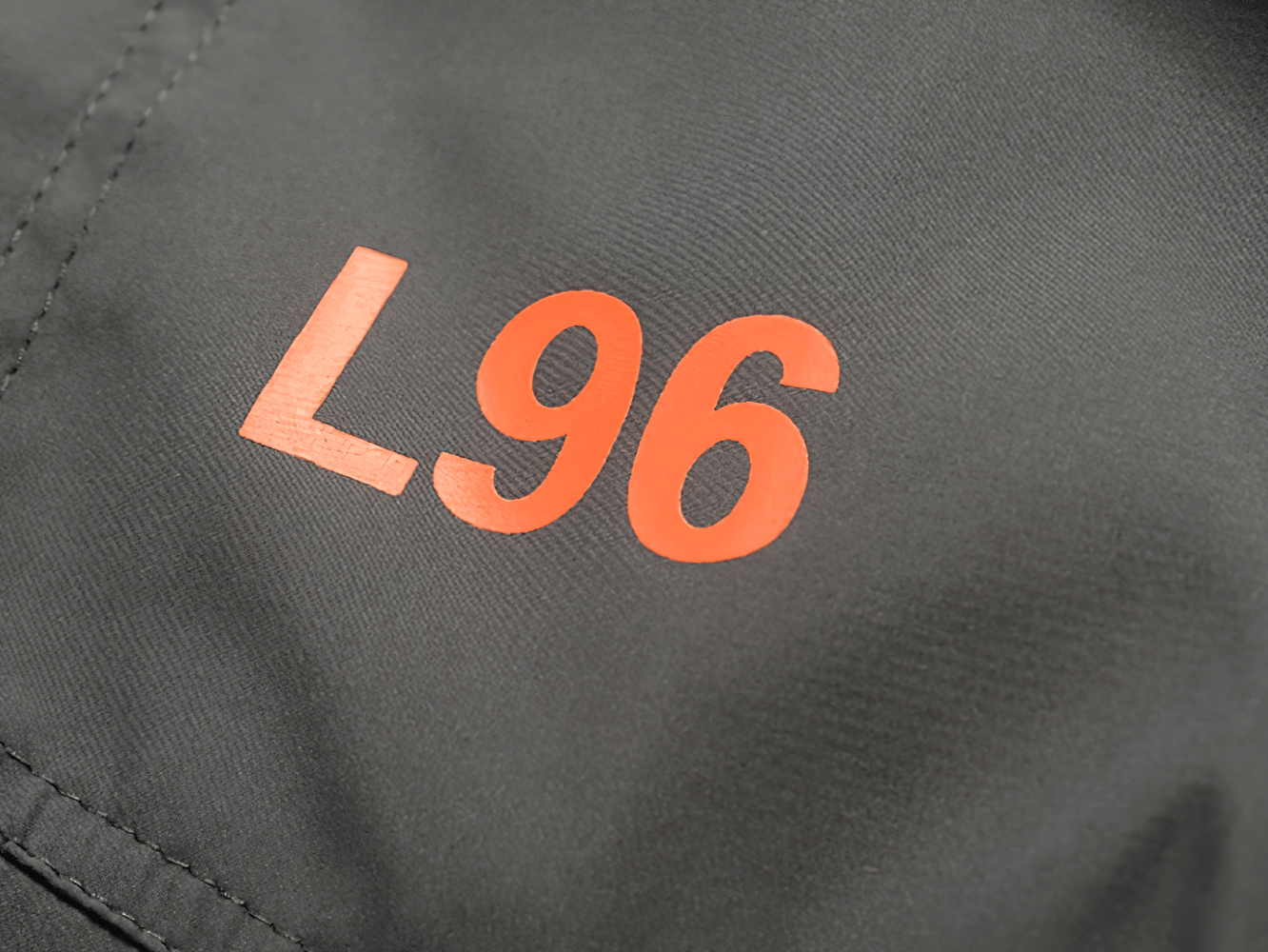 Close-up of red L96 print on black polyester tracksuit fabric, highlighting design detail and sporty style.