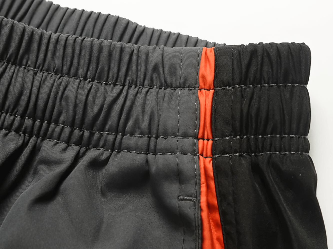 Close-up of men's black tracksuit pants with elastic waist and red stripe detail, showcasing sportswear design and style.