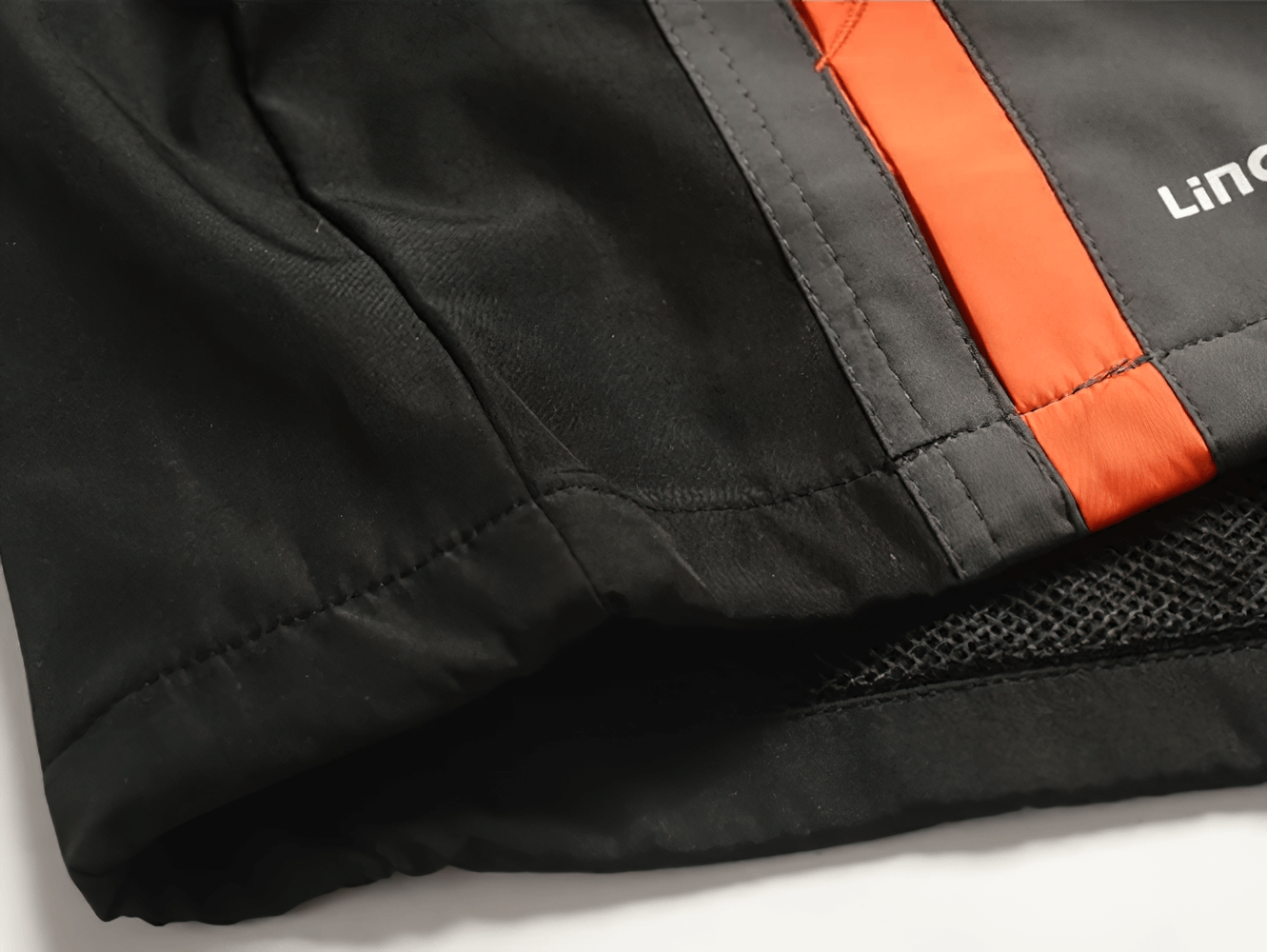 Close-up of a black polyester tracksuit jacket with orange accents, showing detailed stitching and modern design.