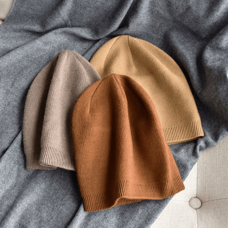 Unisex solid color cashmere wool beanies in brown, beige, and tan shades laid on a cozy grey fabric, perfect for winter warmth and style.