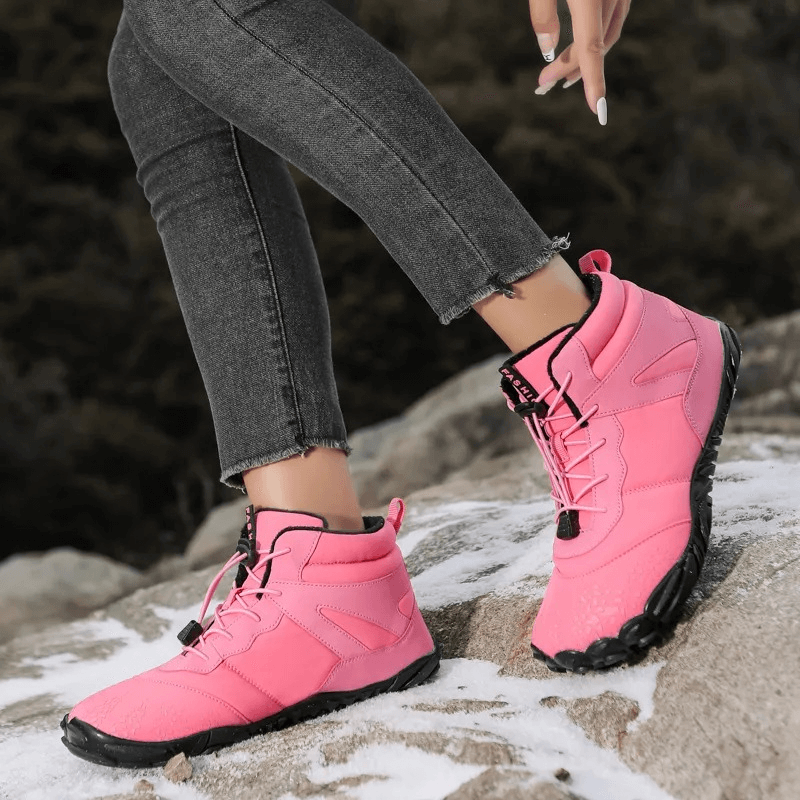 Person wearing pink waterproof hiking boots with black soles, standing on rocky terrain. Casual outdoor fashion footwear.