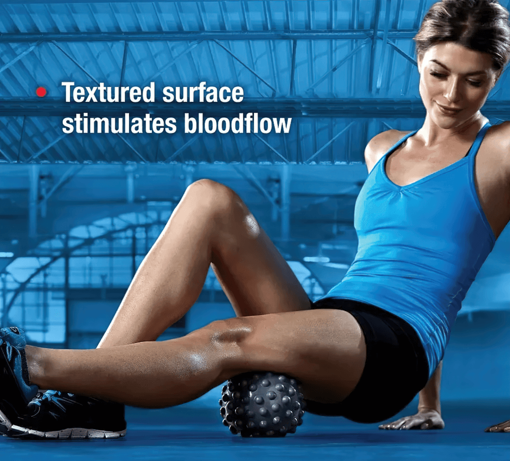 Woman using a vibrating massage ball for muscle tension relief in gym setting, highlighting textured surface for stimulating blood flow.