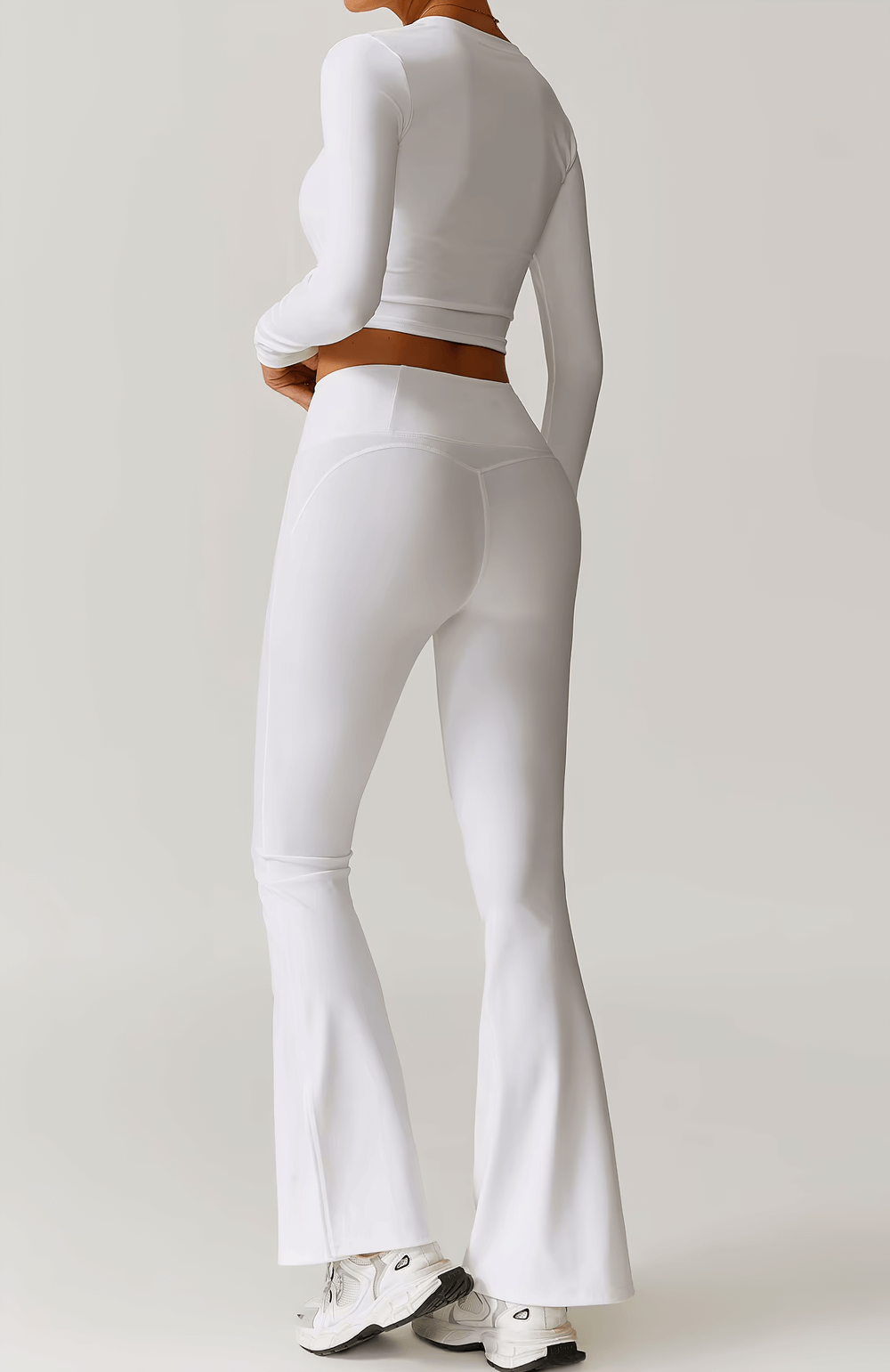 Woman wearing white V-neck long sleeve yoga crop top and flared leggings, showcasing athletic style and comfort.