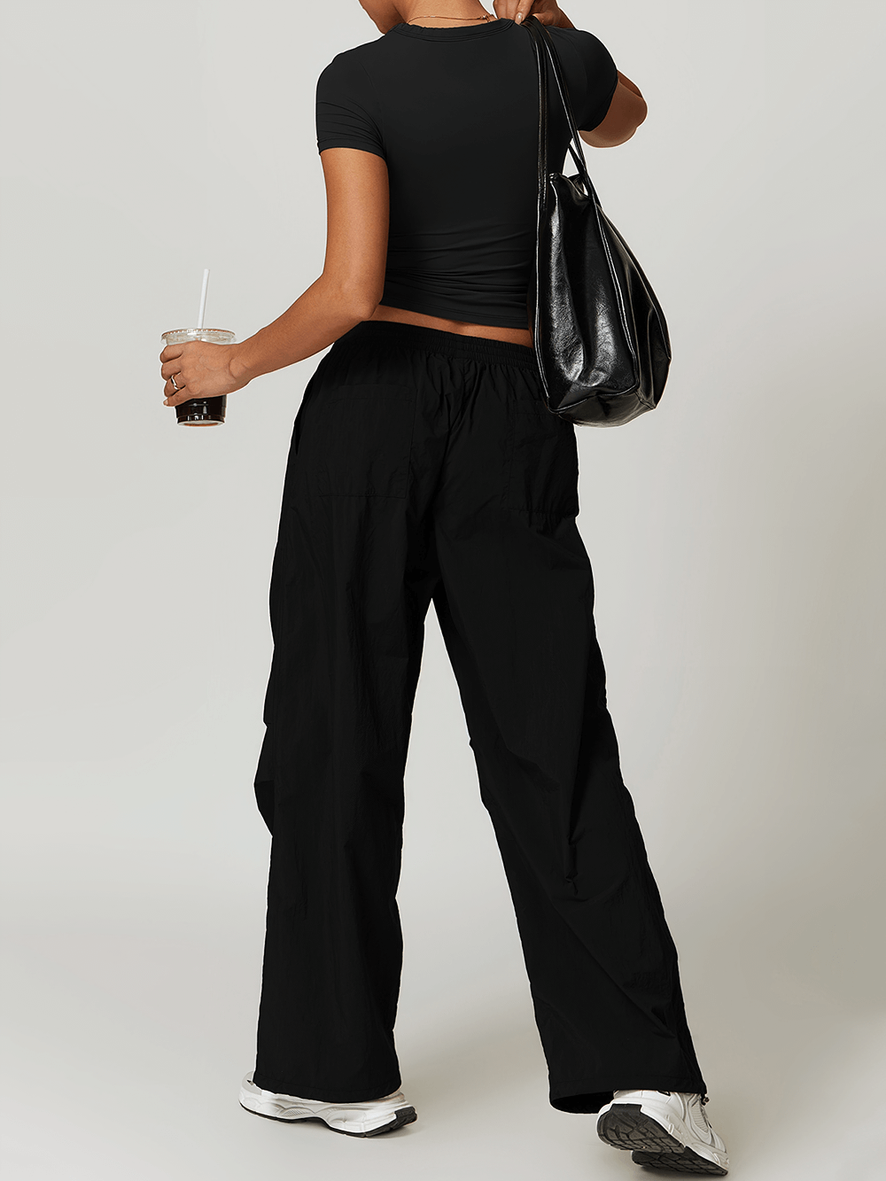 Woman in black sporty outfit holding a drink and carrying a stylish bag, highlighting casual, active lifestyle fashion.