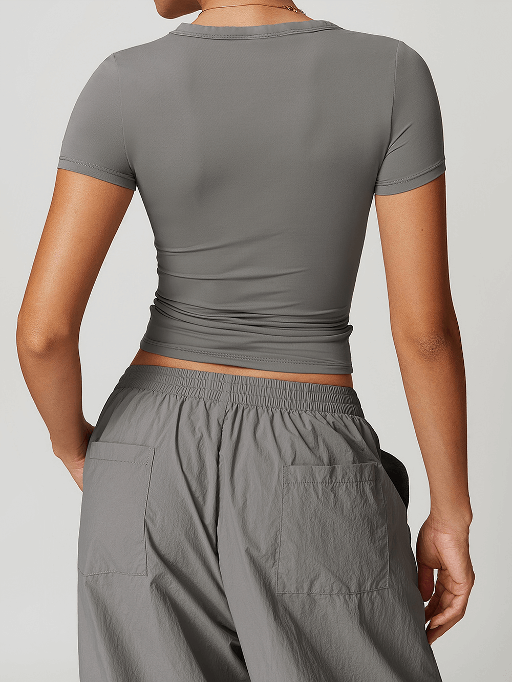 Back view of a woman wearing a gray V-neck yoga tee and relaxed pants, perfect for fitness enthusiasts seeking style and comfort.