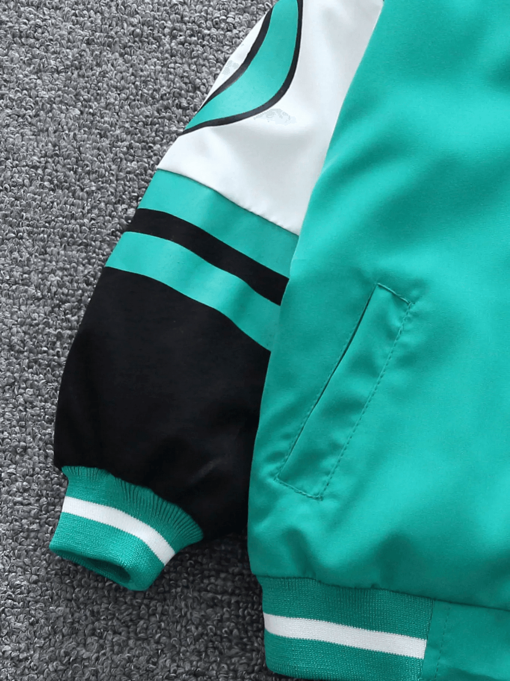 Green and black kids varsity bomber jacket with bold stripes on sleeve, pocket detail, and soft fabric texture.