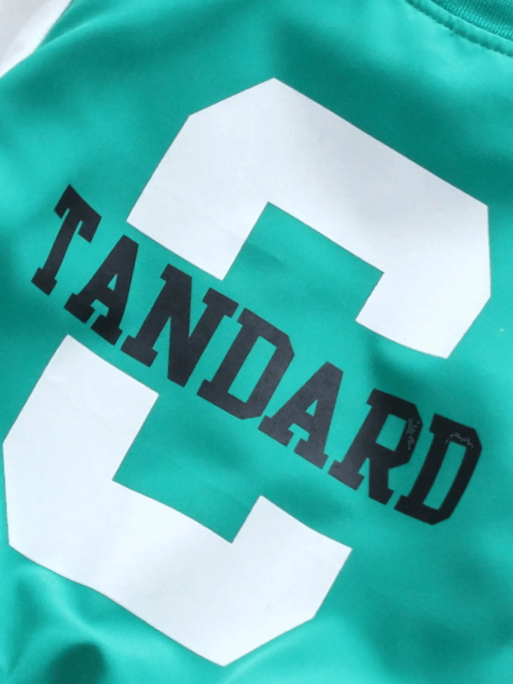 Youth varsity bomber jacket showcasing bold white "C" graphic on a teal background with black lettering.