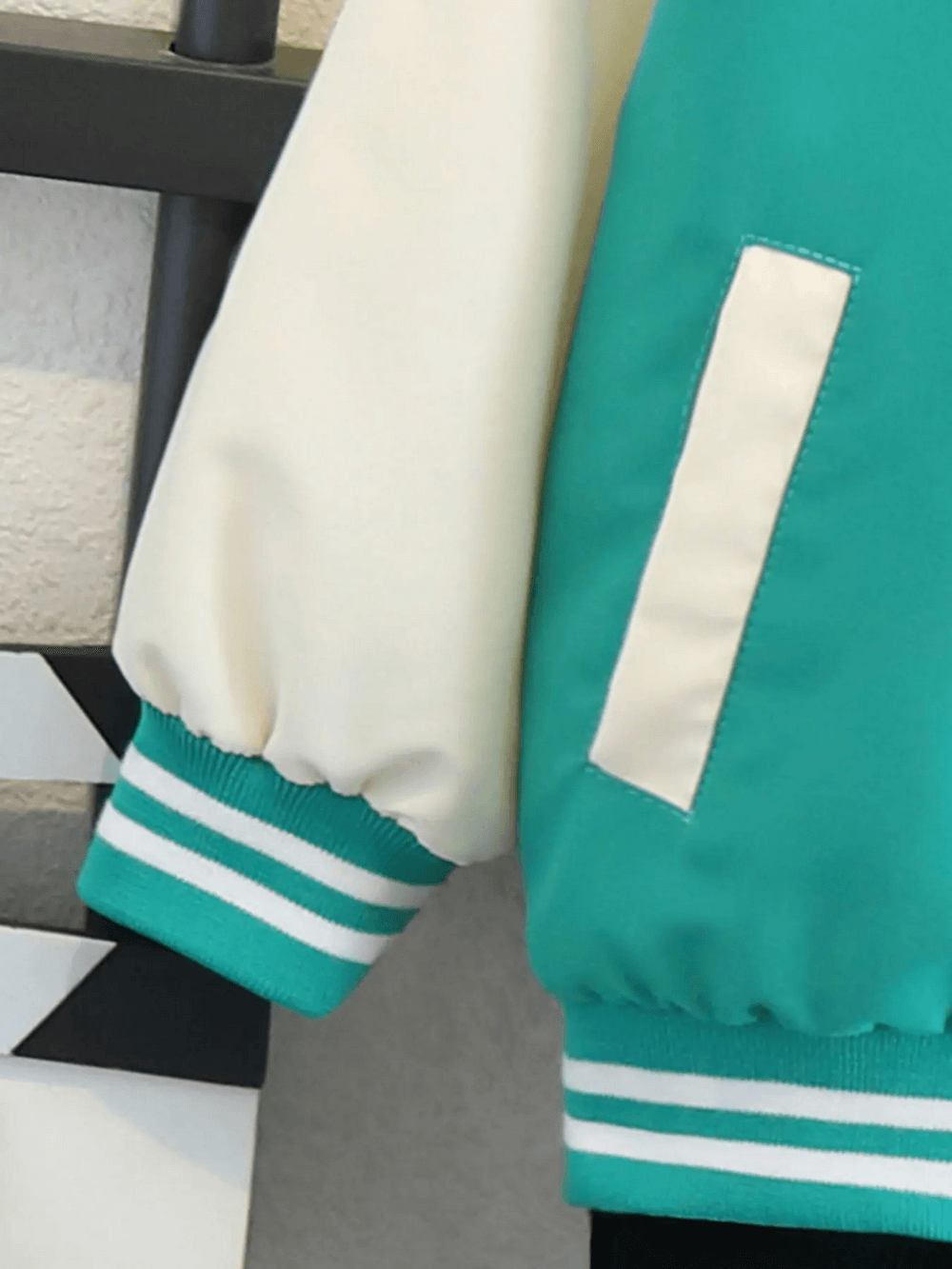 Close-up of a children’s varsity basketball jacket in teal and white color-block with ribbed cuffs.