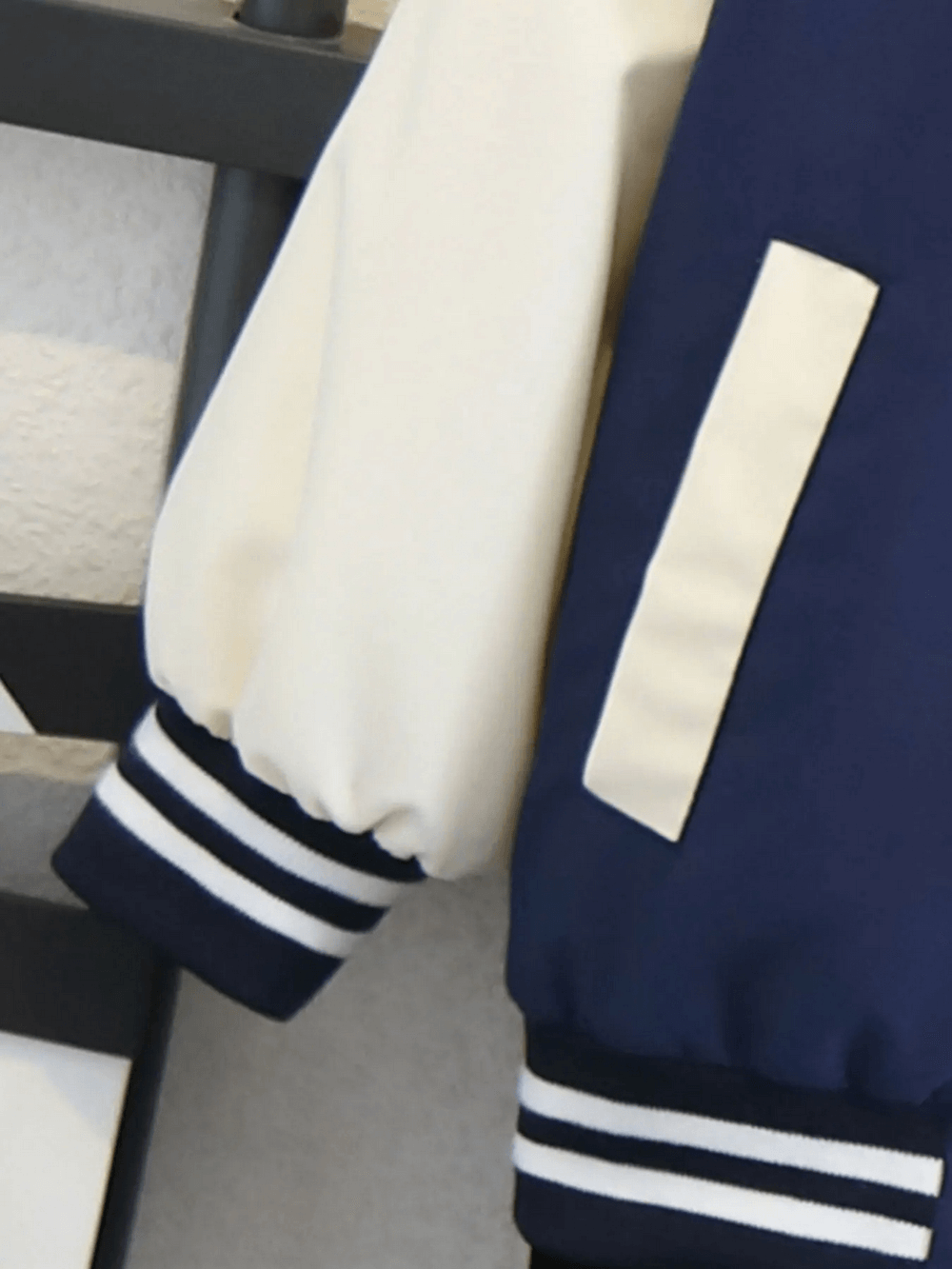 Close-up of a varsity-style basketball jacket sleeve with ribbed cuffs in navy and white.