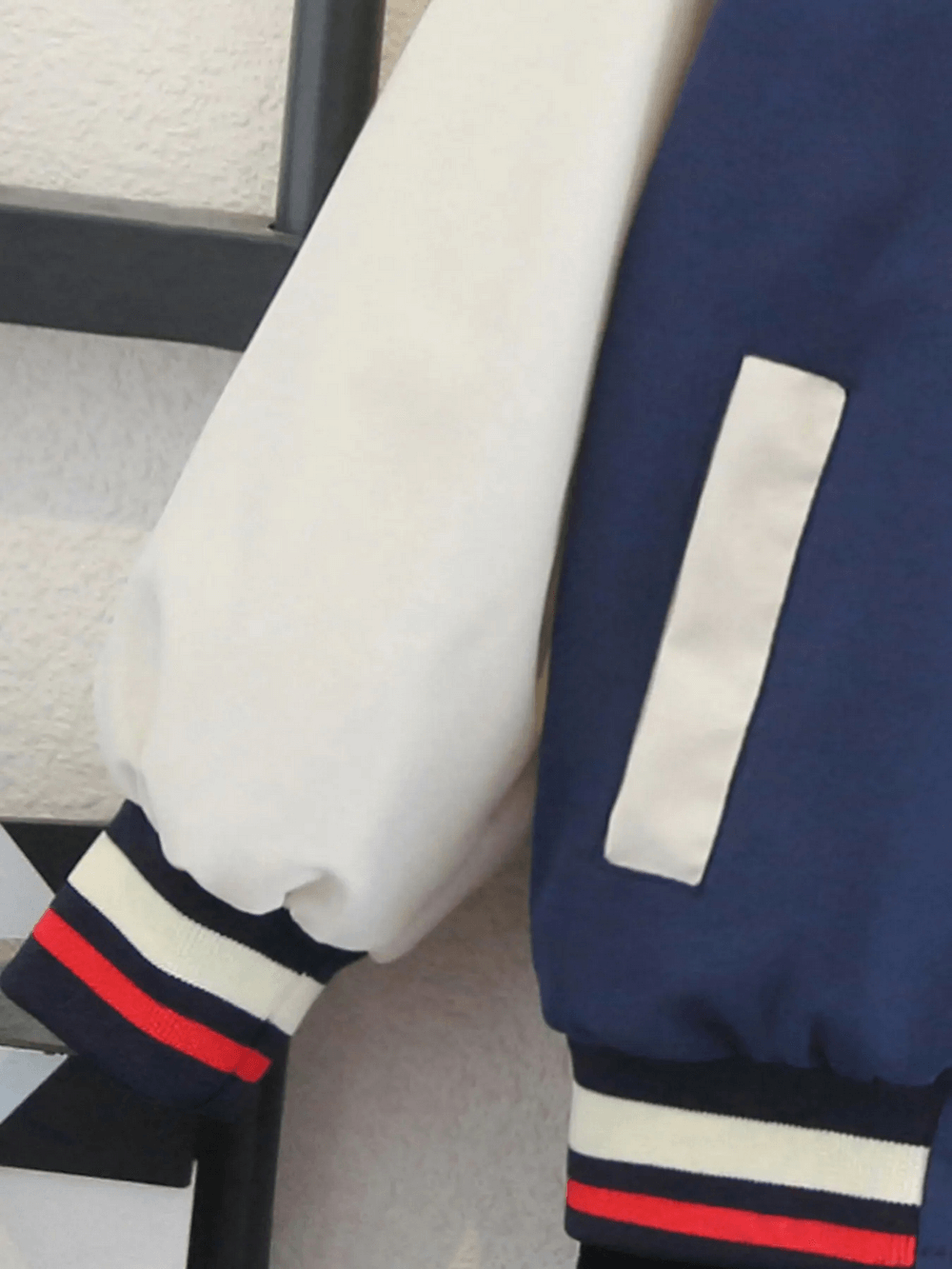Color-blocked kids varsity jacket sleeve detail, featuring navy and beige with ribbed red and white cuffs, ideal for autumn outings.