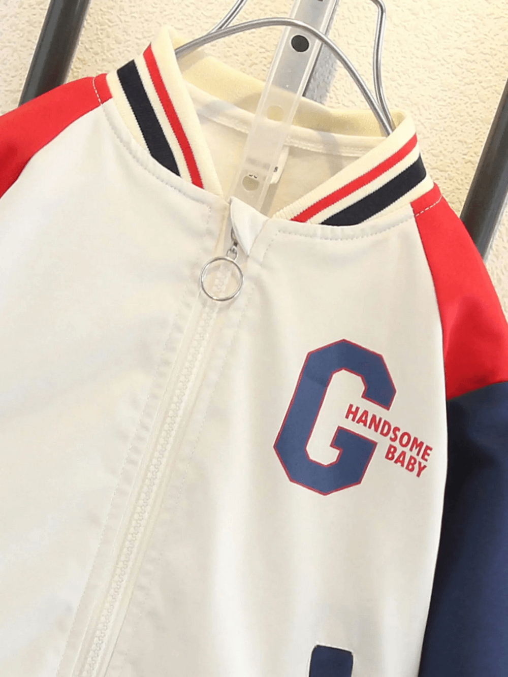 Color-blocked kids varsity jacket with 'G' print and 'HANDsome Baby' text. Features bold red, navy, and beige design for autumn.