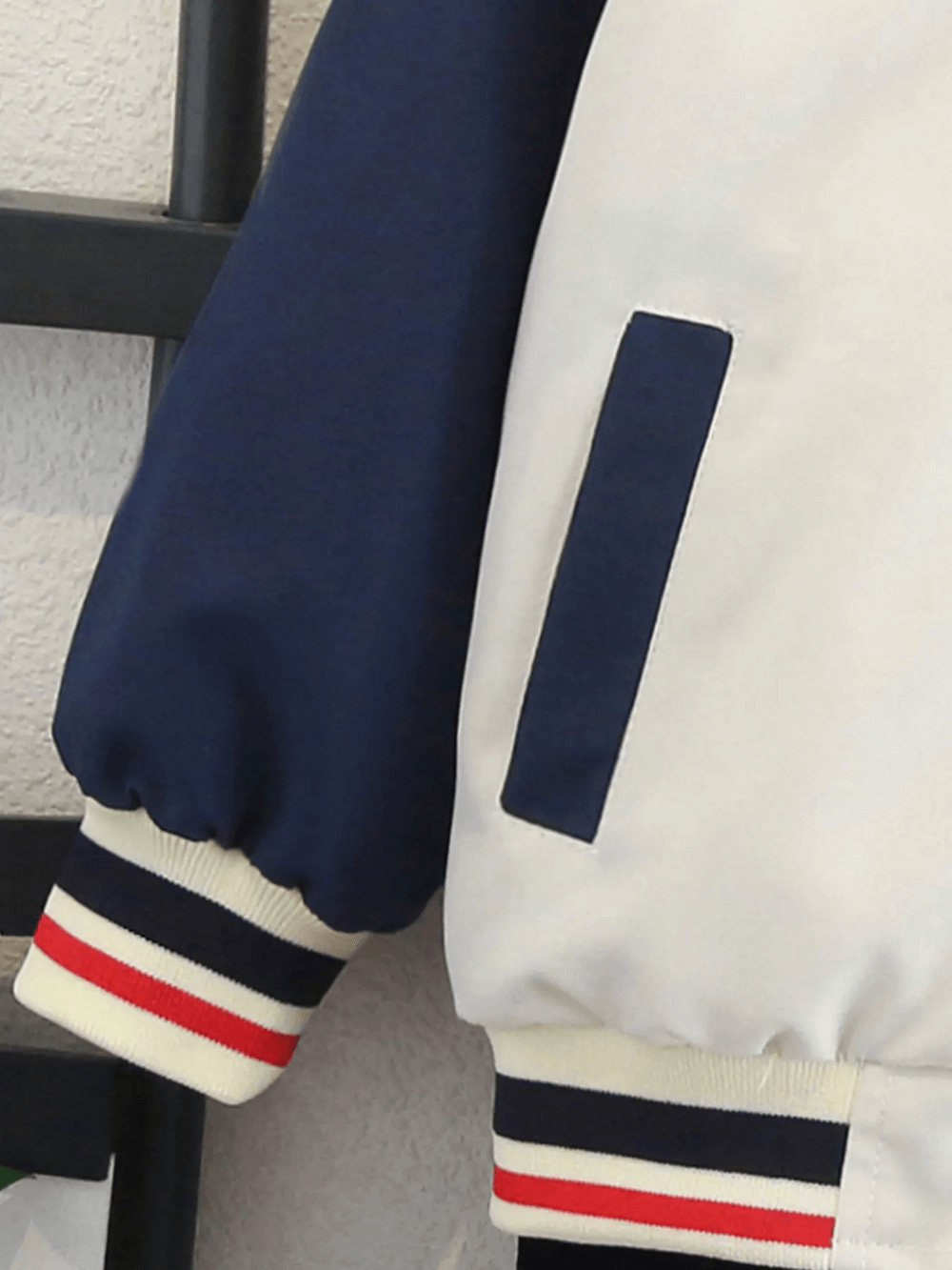 Close-up of kids' varsity jacket with color-blocking in navy, red, and beige featuring ribbed cuffs and pocket detail.