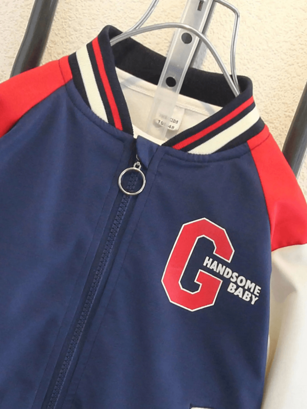 Color-blocked kids varsity jacket with letter 'G' and 'HANDsome Baby' print on chest in navy, red, and beige.