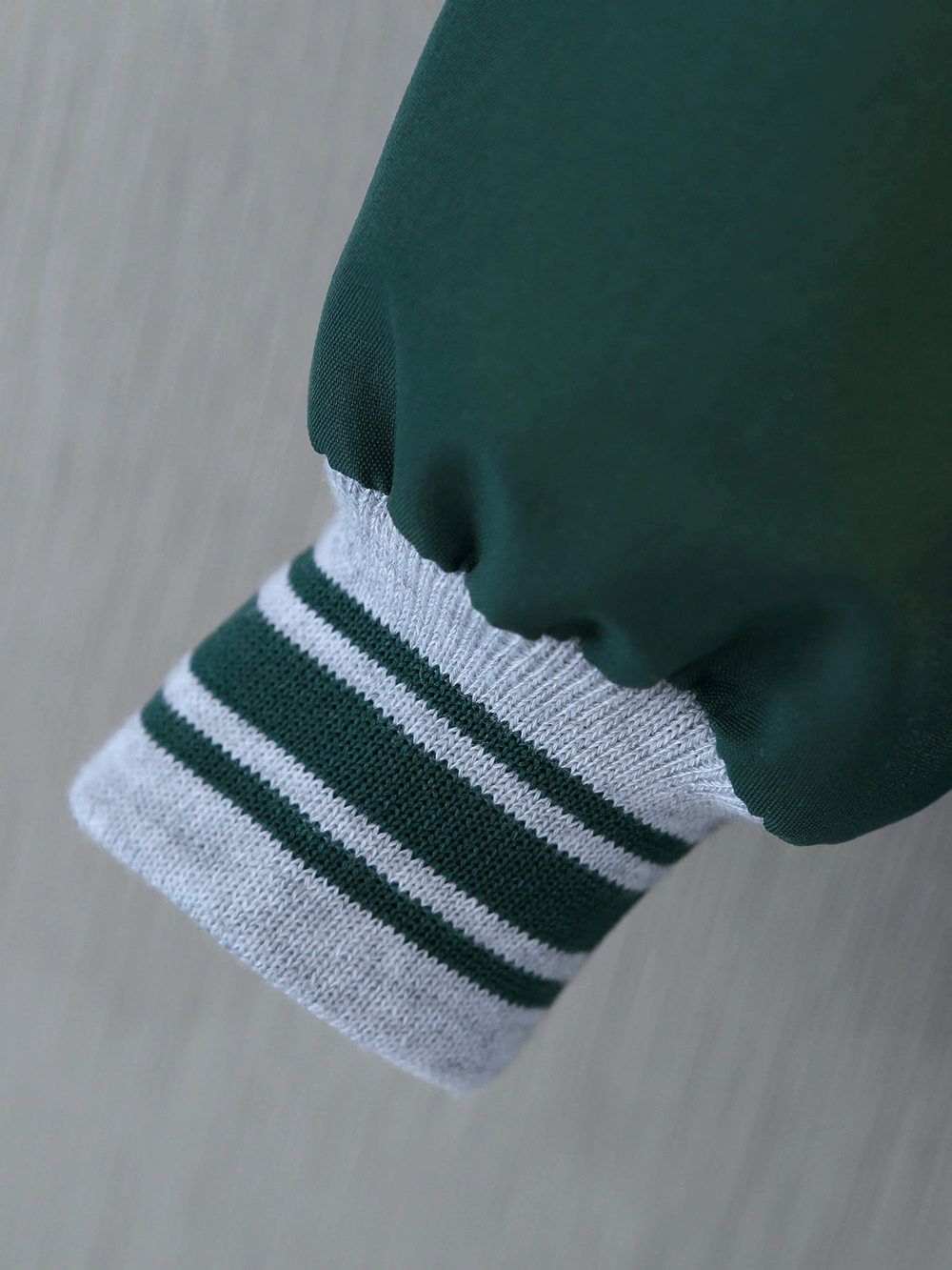 Close-up of teal varsity jacket sleeve with ribbed white and black cuff, showcasing sporty design for kids.