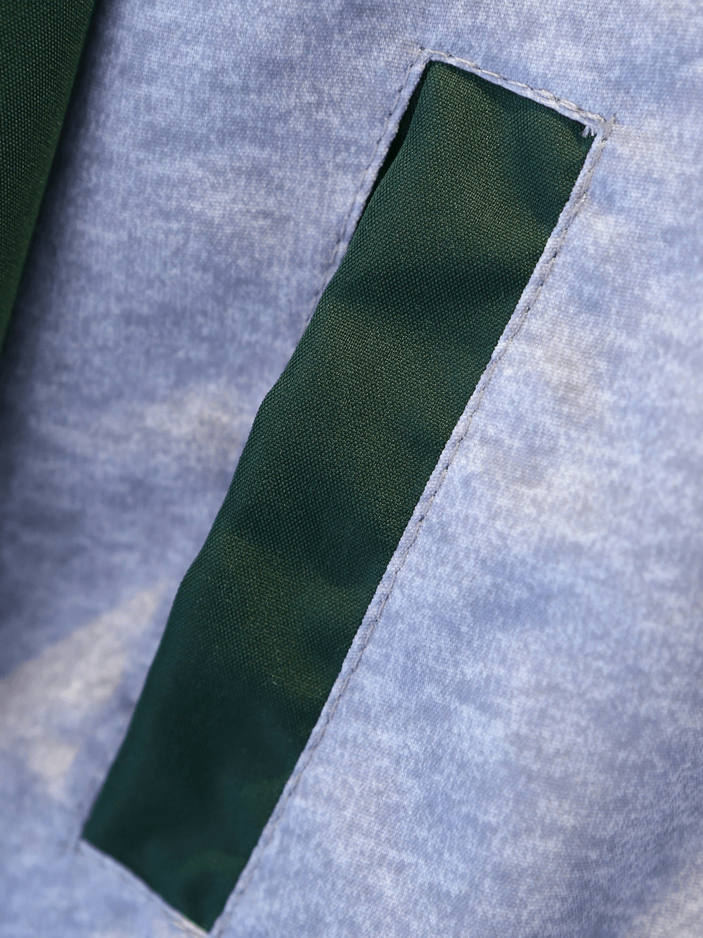 Close-up of a green pocket on a light blue varsity jacket, highlighting fabric texture and stitch detail.