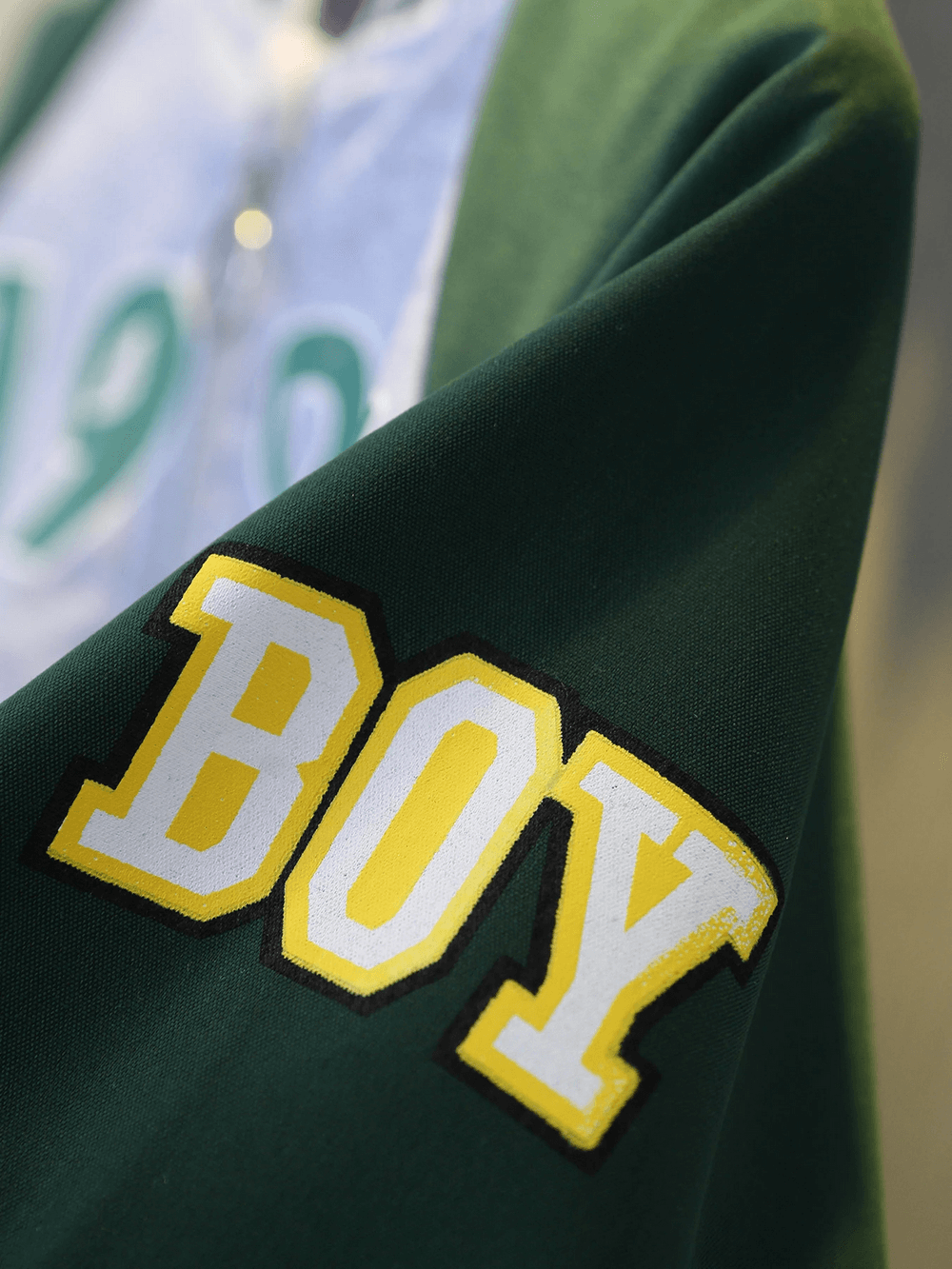 Close-up of a green varsity jacket sleeve with yellow 'BOY' lettering in bold font.