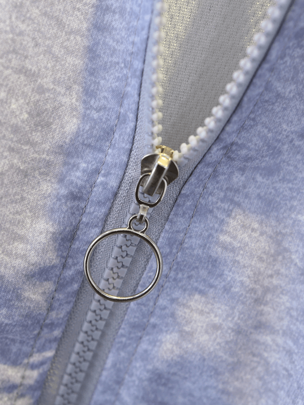 Close-up of a gray zipper with a circular pull tab on fabric background