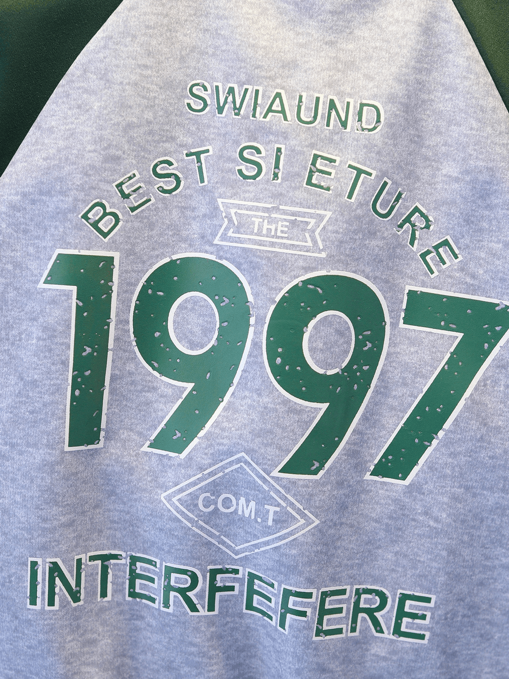 Close-up of a gray sports jacket with green lettering: '1997', 'INTERFERE', and other text.