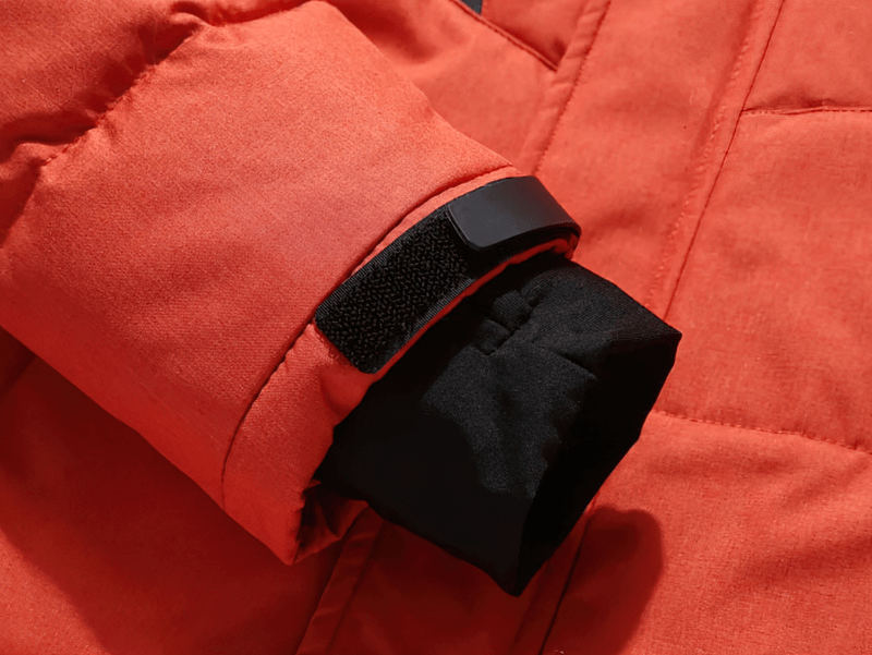 Close-up of orange ski suit sleeve with black inner lining and Velcro strap, showcasing windproof, waterproof outdoor design.