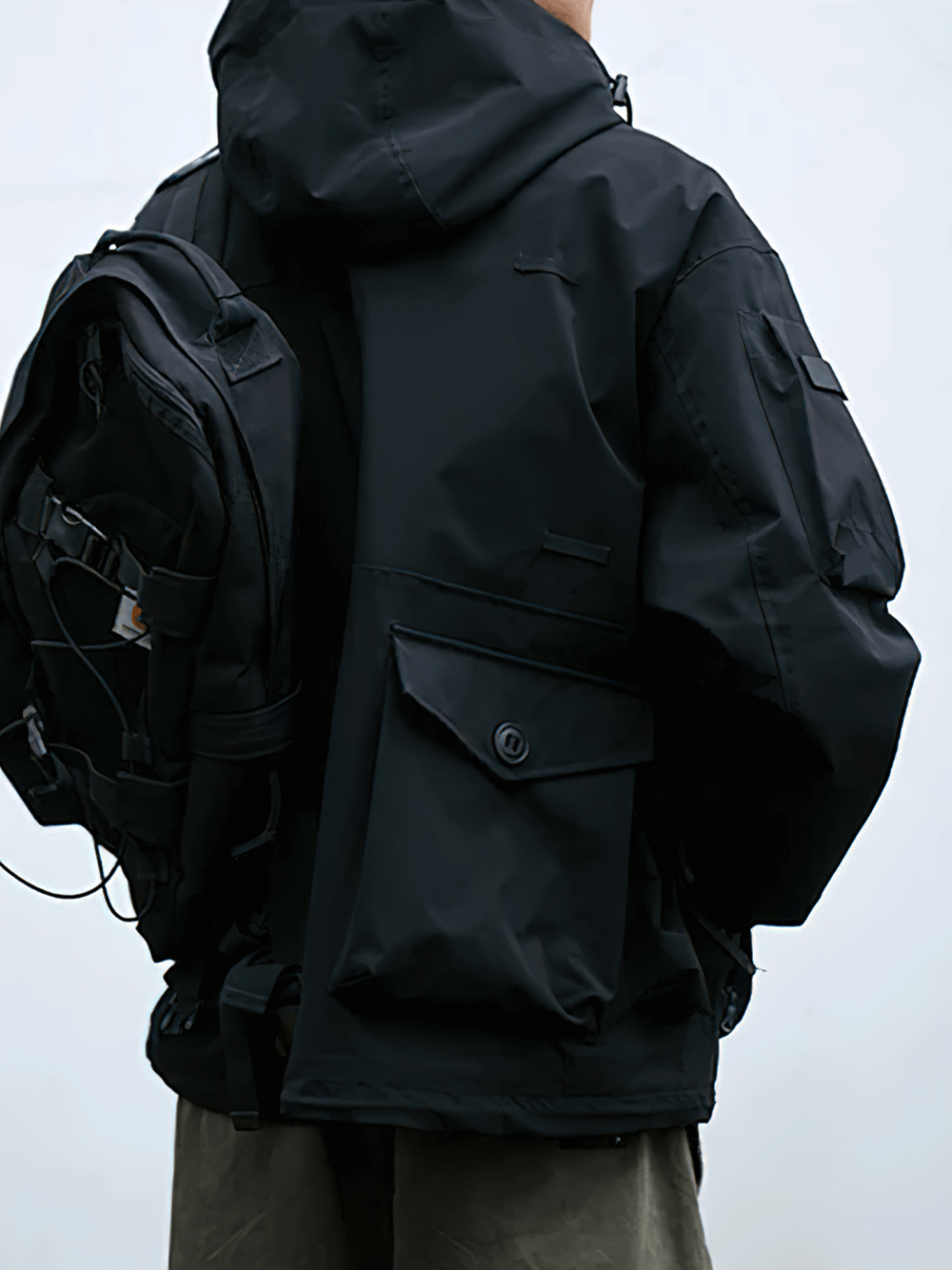 Person wearing a black waterproof hooded outdoor jacket with multiple pockets and backpack, ideal for extreme conditions.