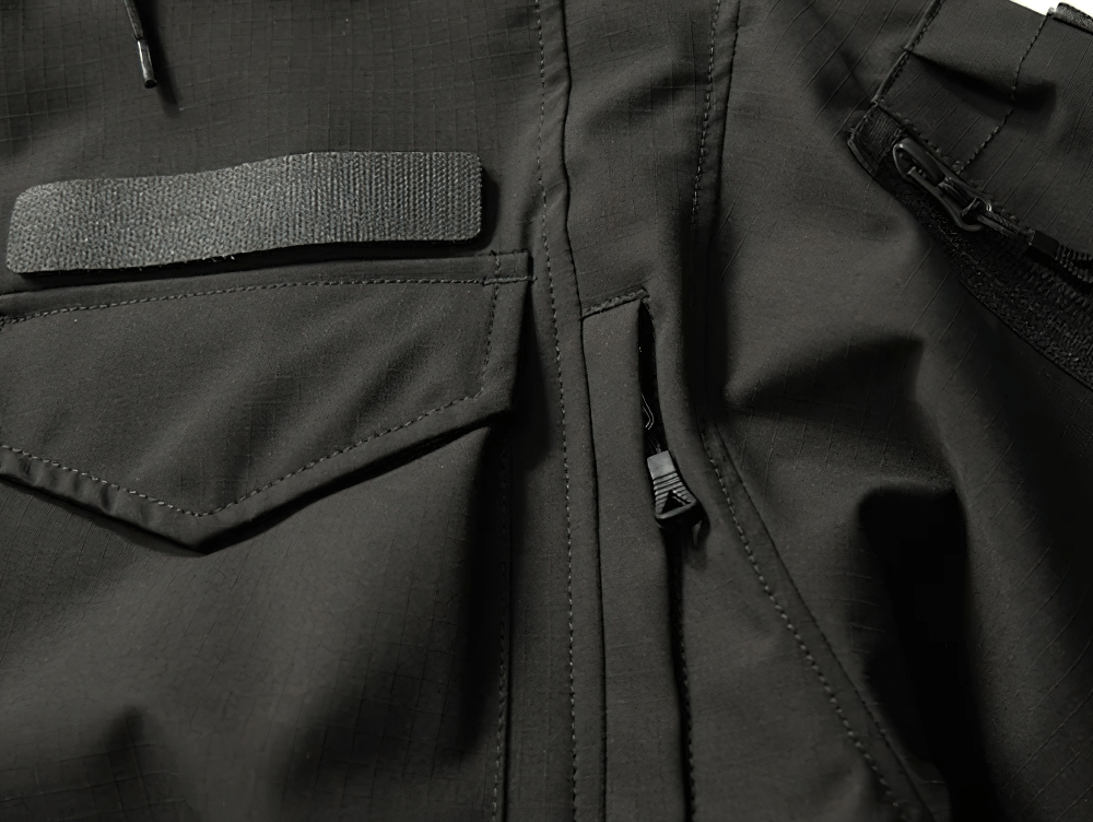 Close-up of black waterproof jacket with multiple utility pockets and zippers, designed for extreme outdoor conditions.