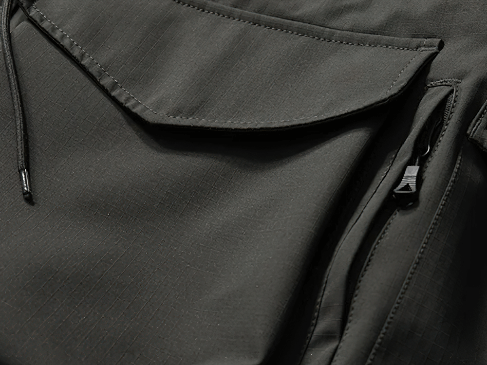 Close-up of black waterproof hooded jacket with multiple pockets, showcasing durable fabric and zippers, ideal for outdoor adventures.